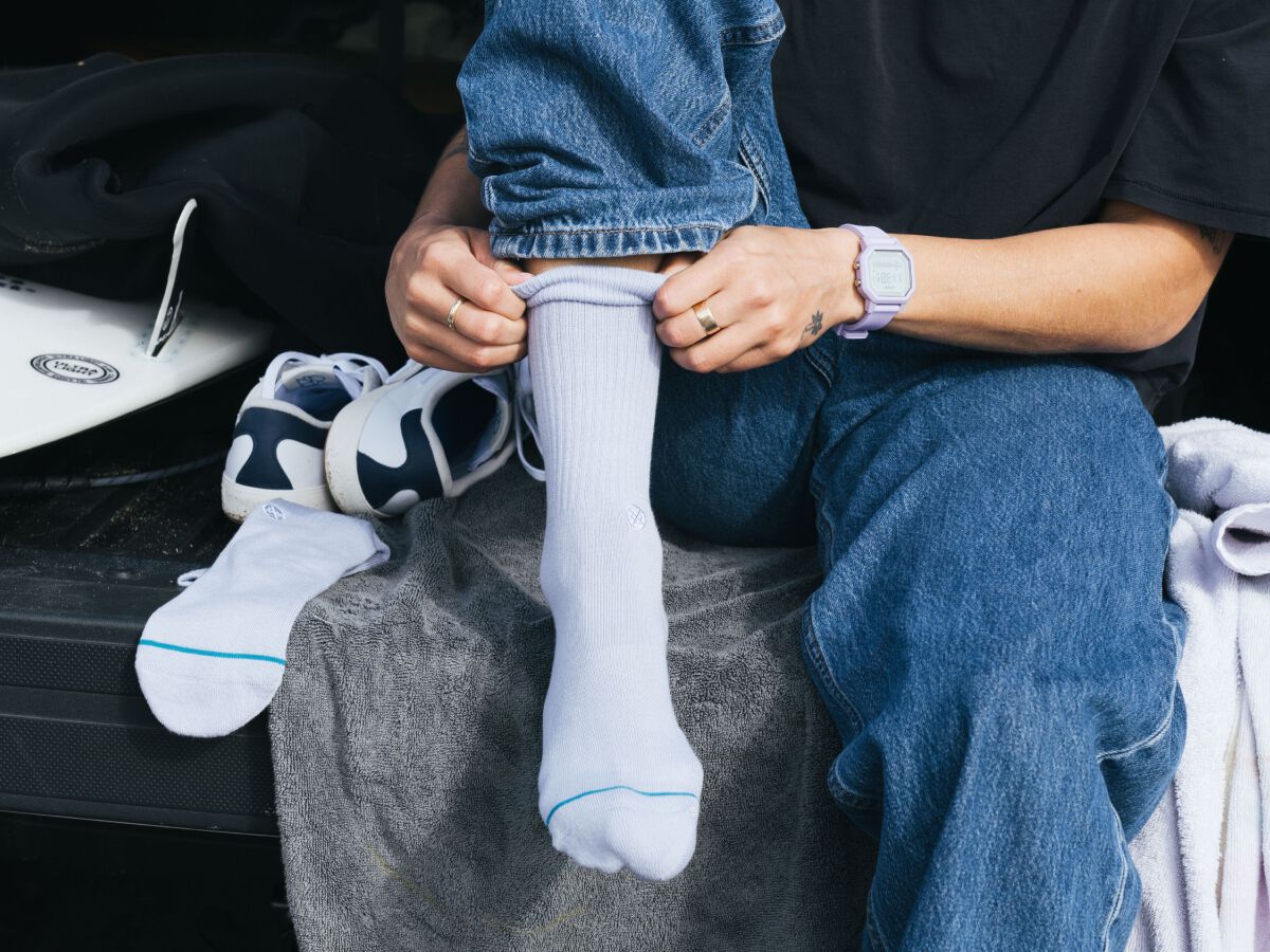 photo of a model putting on a pair of white icon crew socks.