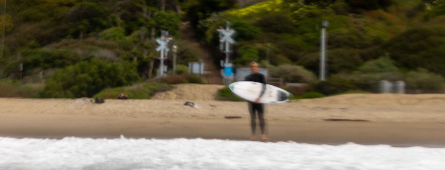 Blurry photo of Cole Houshmand standing on the beach holding his surfboard.